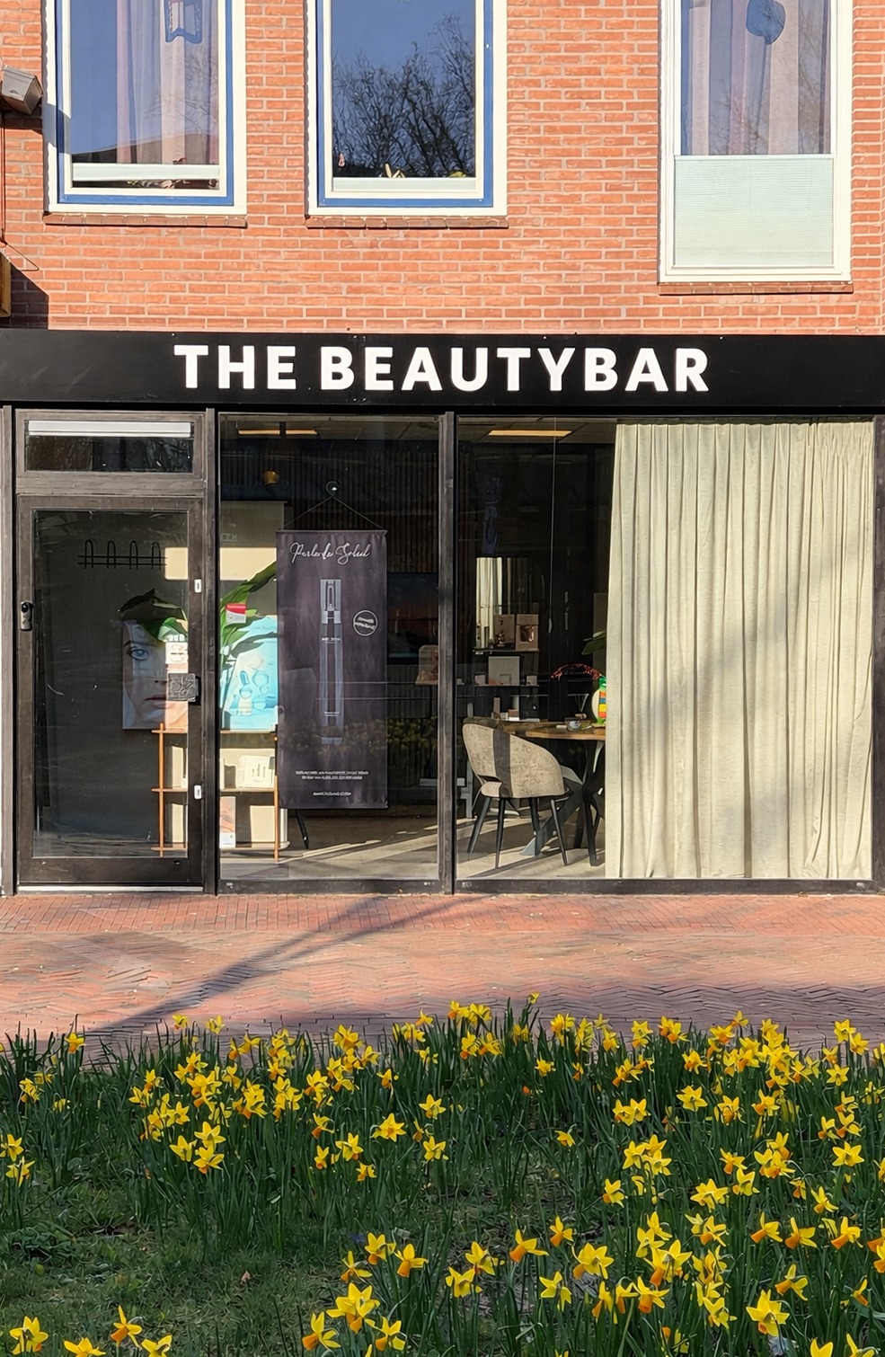 De gevel van The Beautybar aan de Kerkstraat met de zwarte naambord en narcissen ervoor