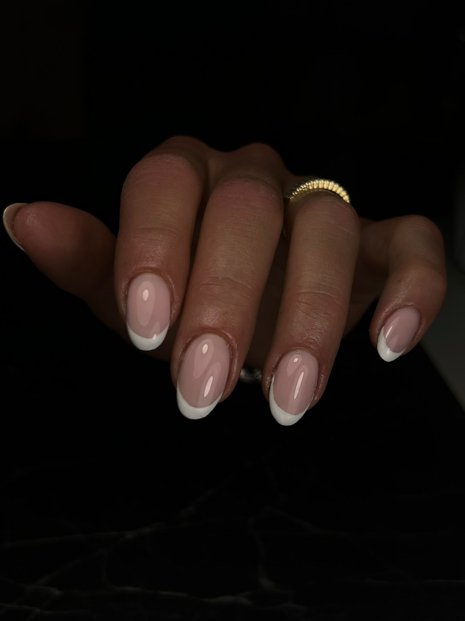 Klassieke French manicure met een gouden ring, tegen een donkere achtergrond