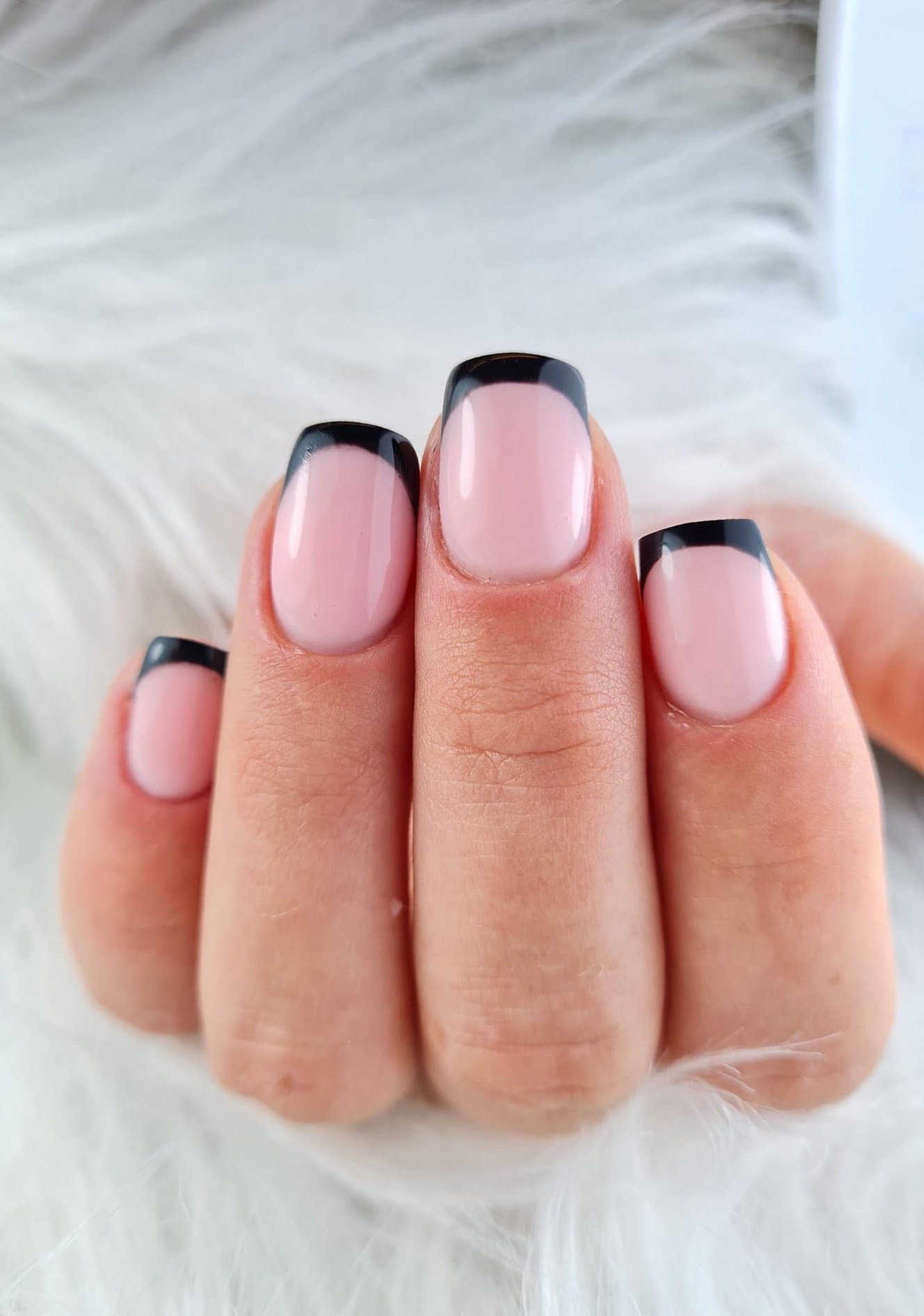 Roze nagels met zwarte French tips op een witte vacht